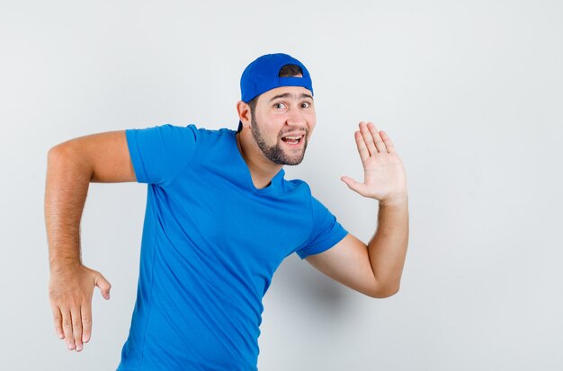 Young man in blue t-shirt and cap gesturing like making movement and looking funny