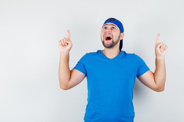 Free photo young man in blue t-shirt and cap pointing up and looking happy