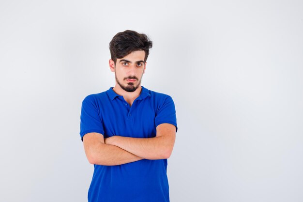 Young man in blue t-shirt standing arms crossed and looking serious