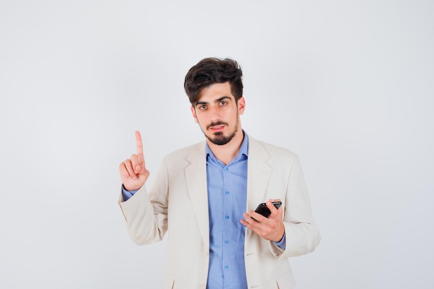 Young man in blue t-shirt and white suit jacket holding smartphone and raising index finger in eureka gesture and looking sensible