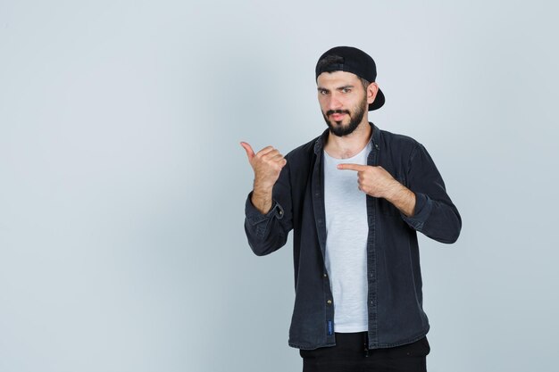 Young man in cap pointing with finger and showing thumbs up