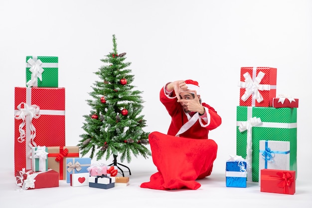 Young man celebrate christmas holiday sitting in the ground near gifts and decorated xmas tree