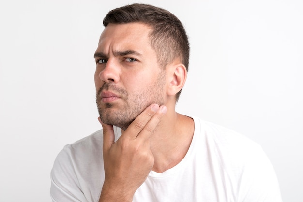 Free photo young man checking his face standing against white wall