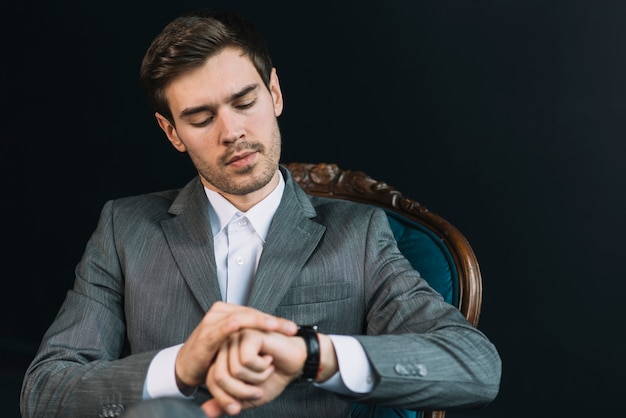 Free photo young man checking time on his watch against black background