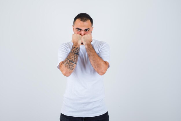 Young man clenching fists in white t-shirt and black pants and looking serious