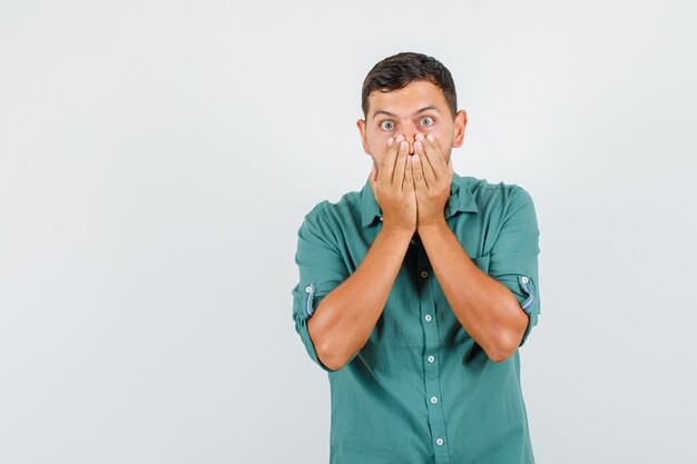 Young man covering mouth with hands in shirt and looking surprised