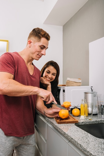 Free Photo young man cutting orange in kitchen with woman