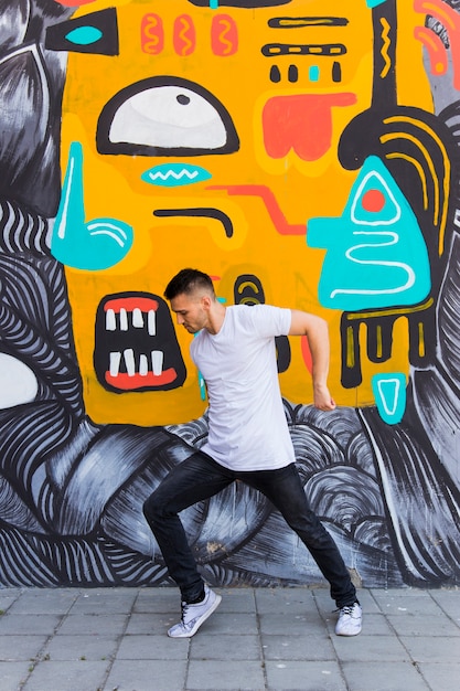 Free photo young man dancing against graffiti wall