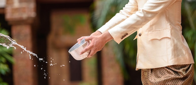 Young man dressed in beautiful Thai costumes enjoy splashing water from bowl in Temple and preserve the good culture of Thai people during Songkran festival Thai New Year Family Day in April