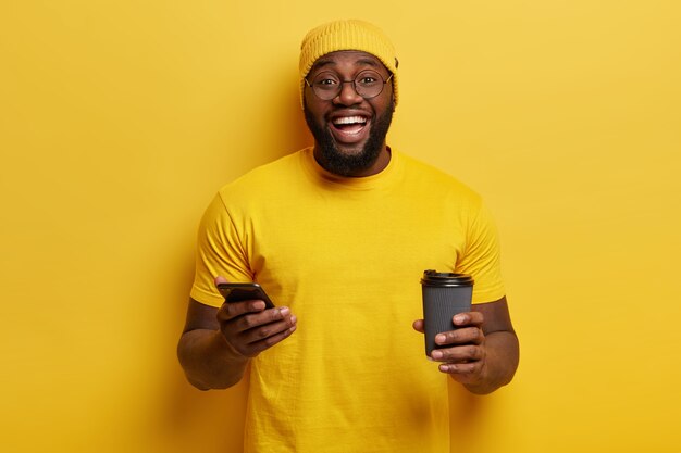 Young man dressed in yellow holding phone and coffee cup