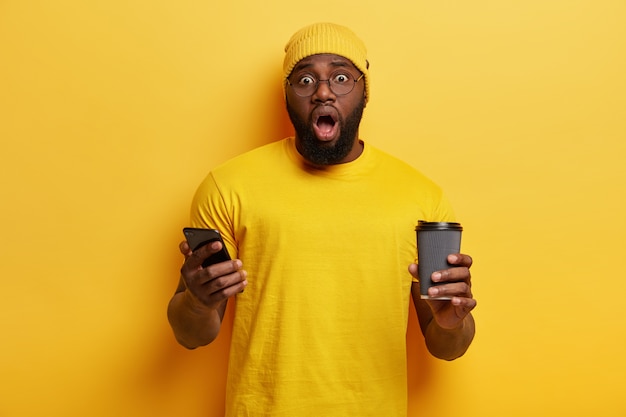 Young man dressed in yellow holding phone and coffee cup