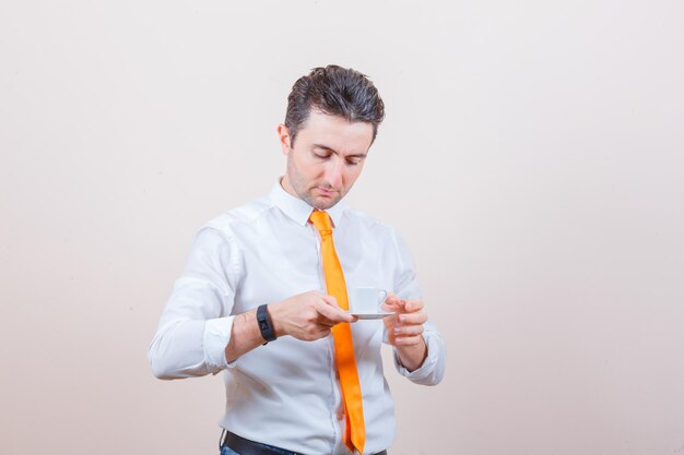 Young man drinking turkish coffee in white shirt, tie and looking careful