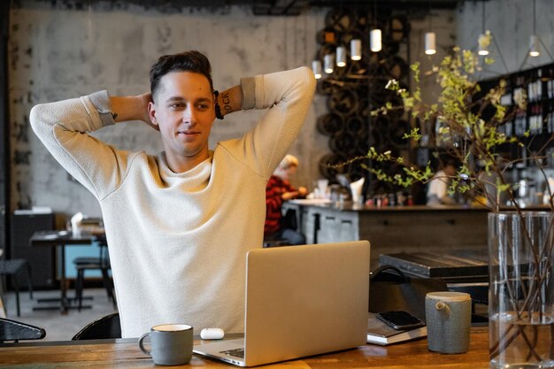 young man drinks tea and works on a laptop, freelancer working in a cafe