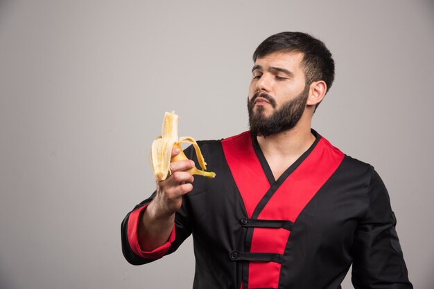 Young man eating a banana on gray wall.