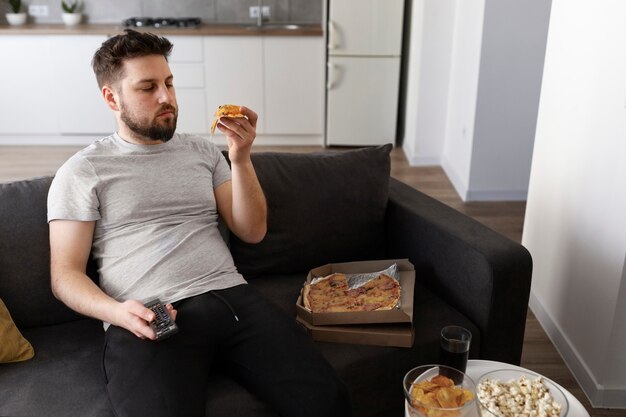 Young man eating junk food at home on the sofa