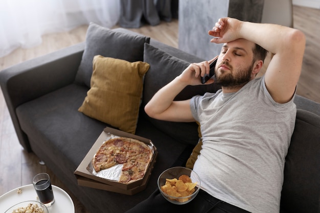 Young man eating junk food at home on the sofa