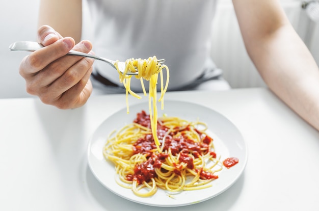 Young man eating tasty spaghetti with tomato sauce. Closeup.