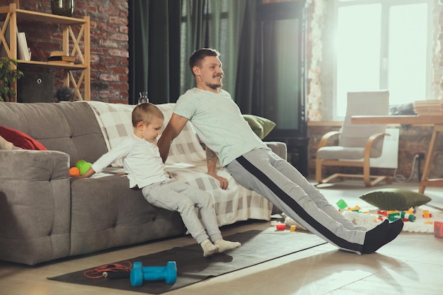 Young man exercising fitness aerobic yoga at home sporty lifestyle Getting active while his child playing on the background home gym