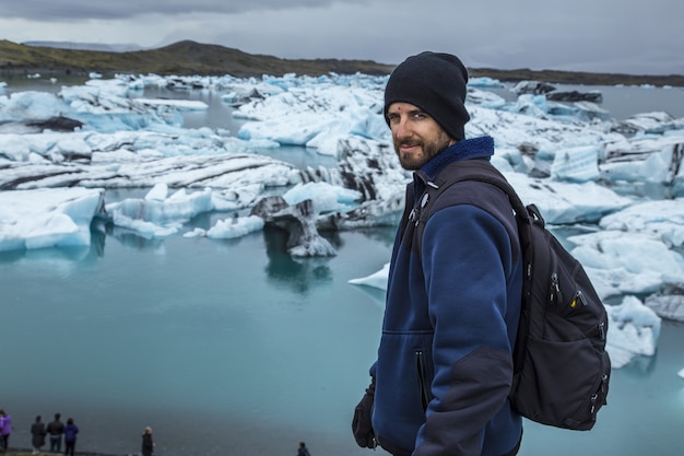 Free photo young man in front of small blue icebergs in jokulsarlon ice lake and very gray sky in iceland