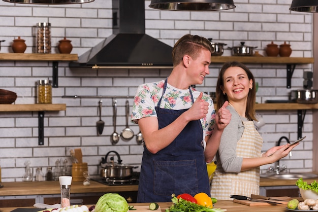 Young man gesturing thumb up to girlfriend while cooking together