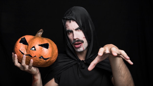 Free photo young man in halloween costume posing with jack o'lantern