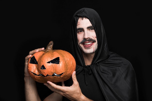 Free photo young man in halloween costume posing with pumpkin