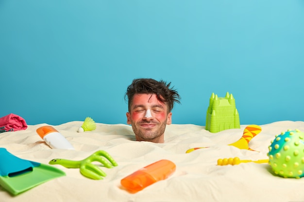 Young man head with sunscreen cream on face surrounded by beach accessories