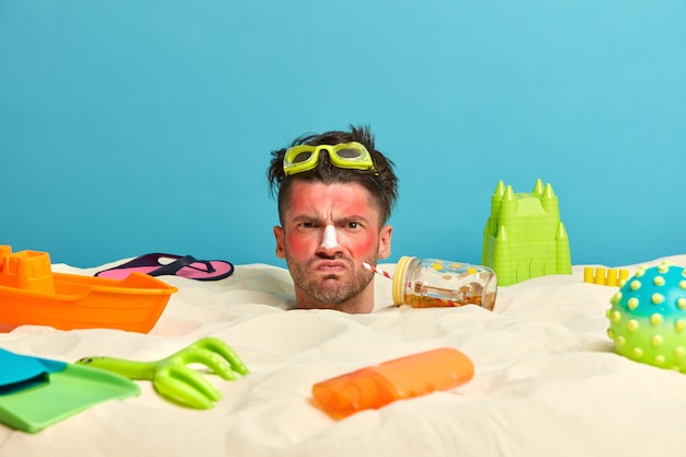 Free photo young man head with sunscreen cream on face surrounded by beach accessories