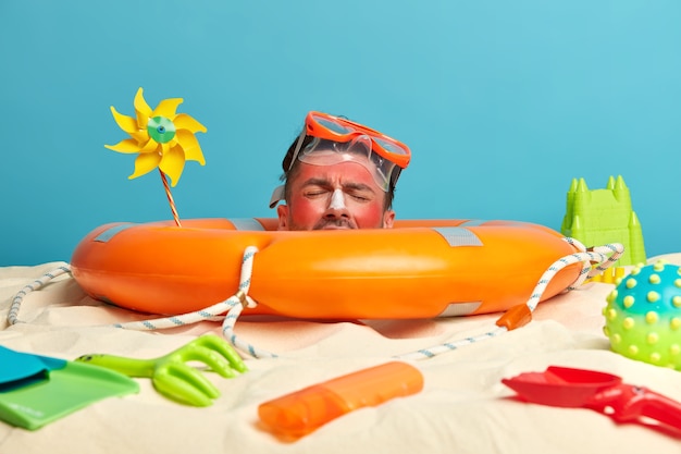 Free Photo young man head with sunscreen cream on face surrounded by beach accessories