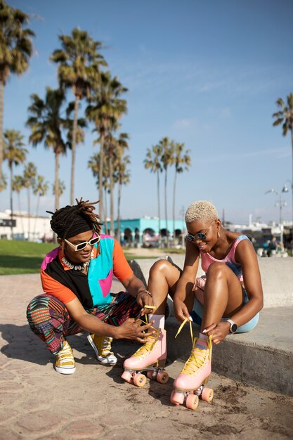 Young man helping his friend tying her roller skates outside in the park