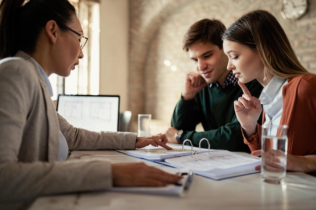 Young man and his wife examining housing plans with real estate agent on a meeting in the office