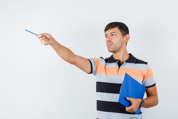 Young man holding clipboard while pointing away in t-shirt and looking focused