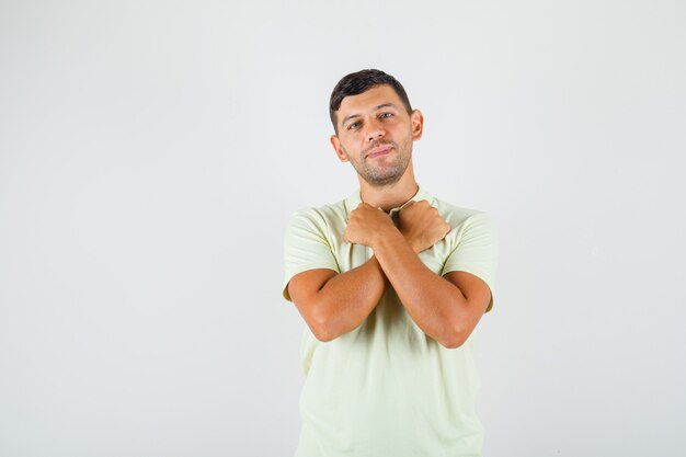 Young man holding crossed fists near his neck in t-shirt and looking happy