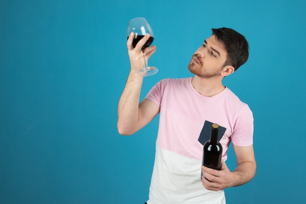 Young man holding glas of wine up and looking at it.