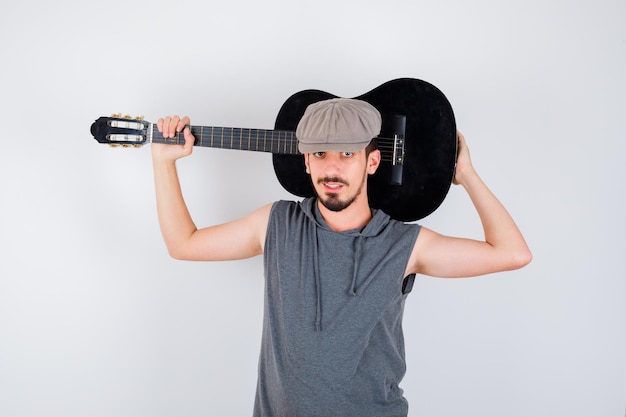 Free photo young man holding guitar in gray t-shirt and cap and looking handsome