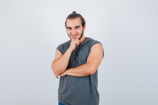 Young man holding hand on chin in hooded t-shirt and looking pleased , front view.