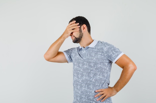 Young man holding hand on eyes in t-shirt and looking embarrassed. front view.