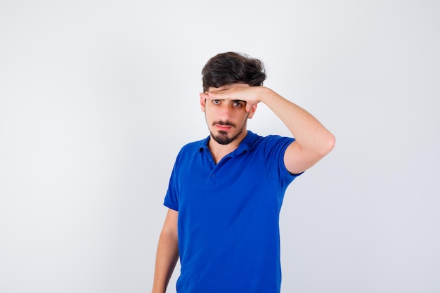 Young man holding hand on forehead in blue t-shirt and looking serious