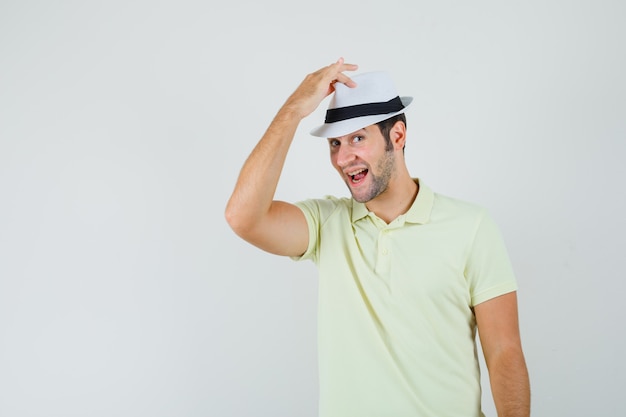 Young man holding hand on his hat in t-shirt and looking handsome 