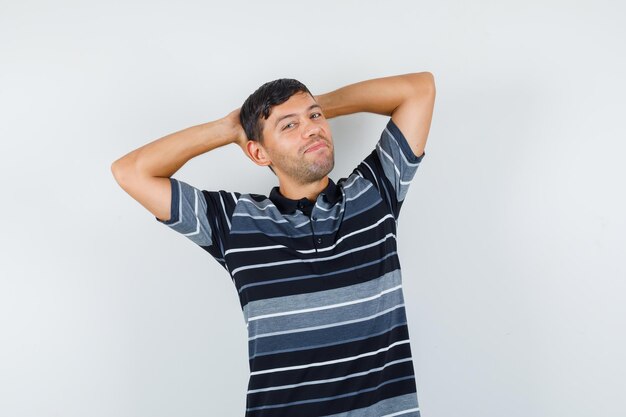 Young man holding hands behind head in t-shirt and looking relaxed , front view.