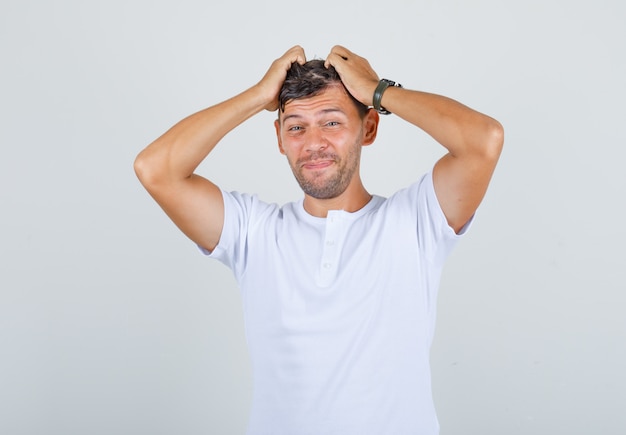 Young man holding hands to his head in white t-shirt and looking sorry, front view.