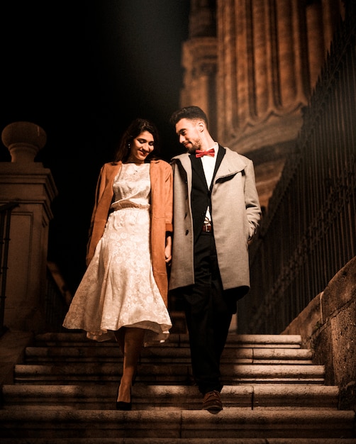 Young man holding hands with happy elegant woman and going down on steps