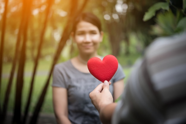 Young man holding heart shaped valentine card and looking while standing  with girlfriend.