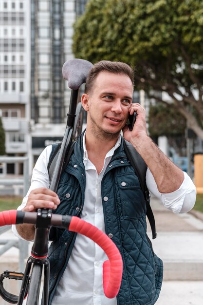 Young man holding his bike and talking on the phone