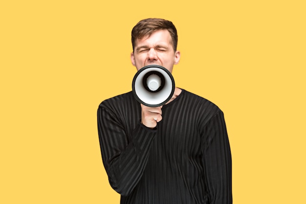 young man holding a megaphone on on yellow studio background