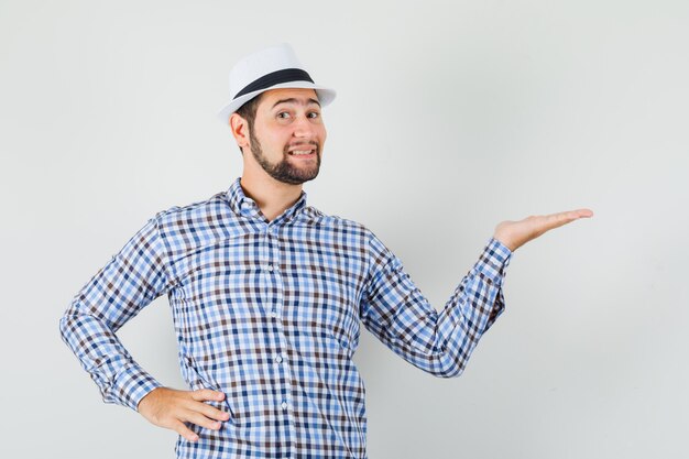 Young man holding palm like showing something in checked shirt