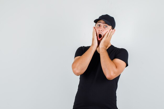 Young man holding palms on cheeks in black t-shirt