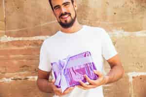 Free photo young man holding present against weathered wall