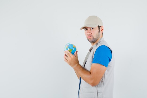 Young man holding school globe in t-shirt, jacket and looking