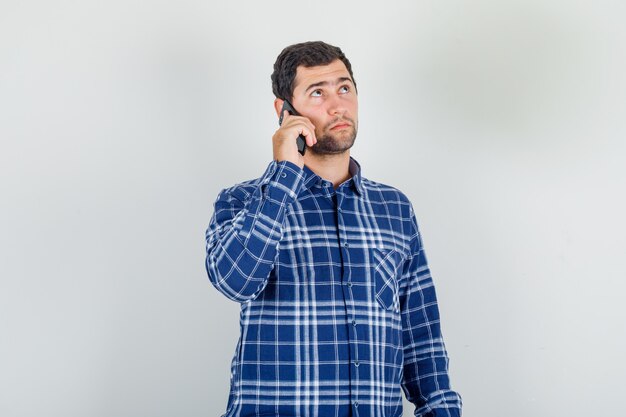 young man holding smartphone and thinking in checked shirt